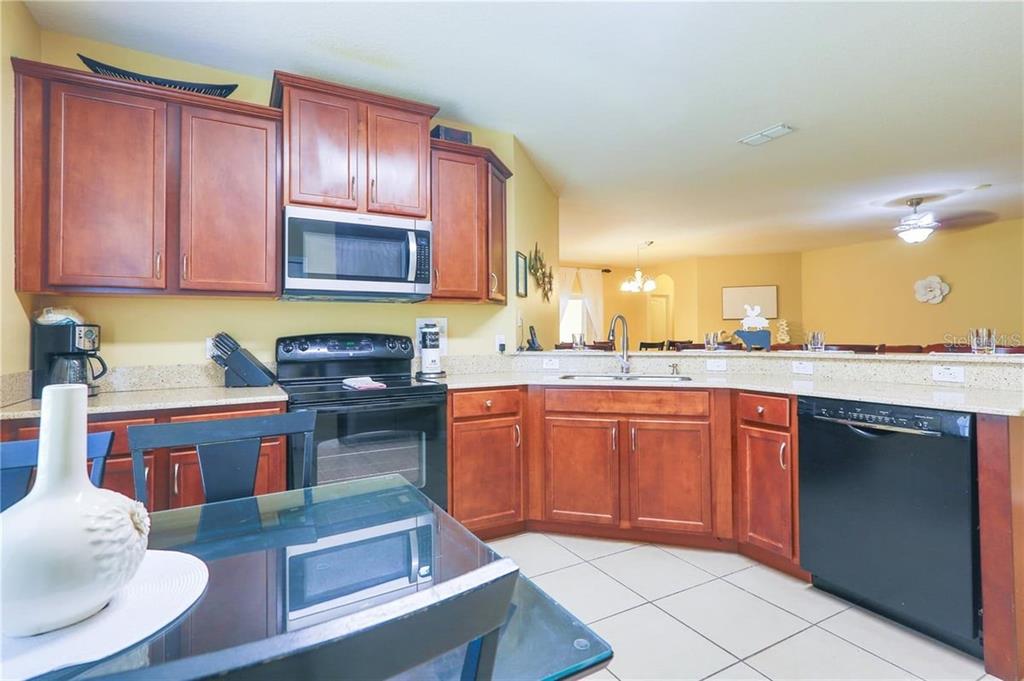 A kitchen with wood cabinets, black appliances, and a glass-topped dining table — 9122 STROMBOLI COURT, KISSIMMEE, FL