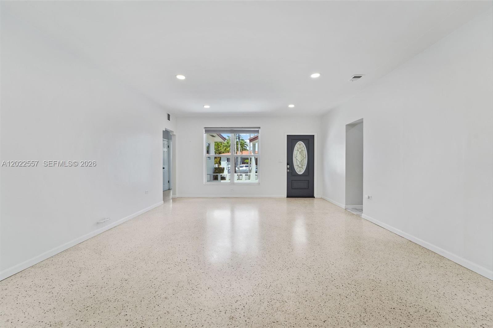 A bright, empty living room features white walls, recessed lighting, and speckled terrazzo flooring — 8927 Carlyle Ave, Surfside FL 33154, SURFSIDE, FL