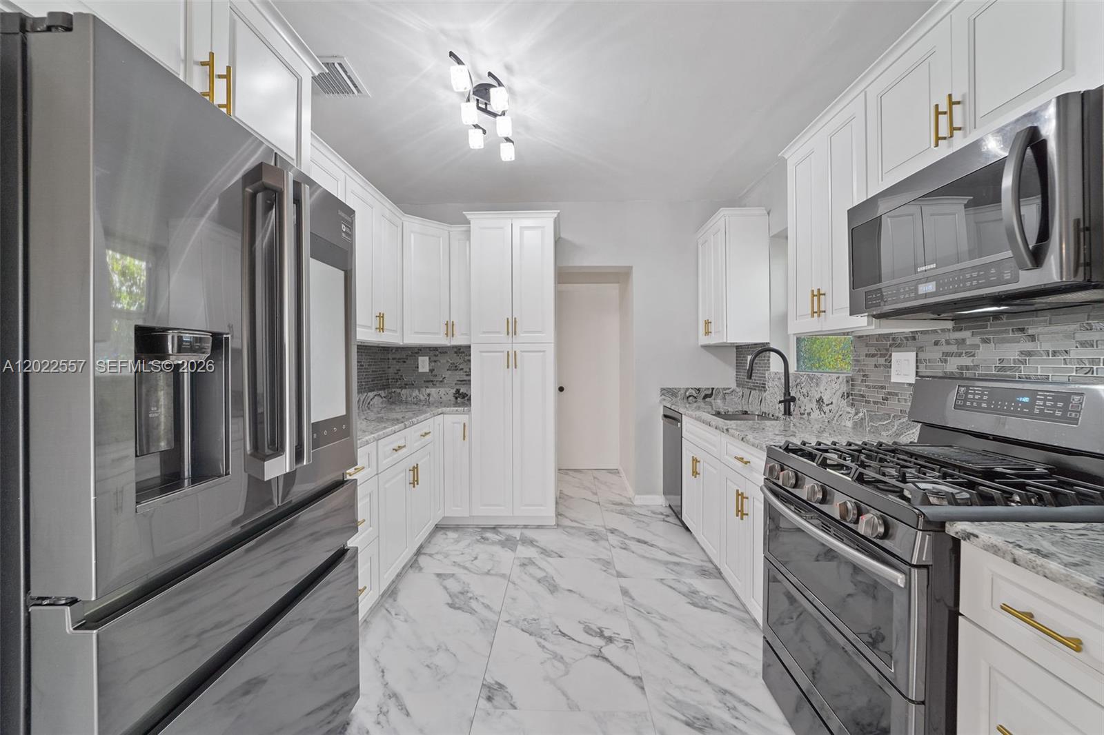 A modern kitchen features white cabinets, stainless steel appliances, marble-patterned tile floors, and gold hardware — 8927 Carlyle Ave, Surfside FL 33154, SURFSIDE, FL