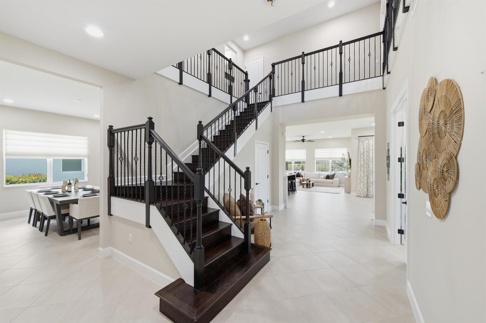 A grand foyer features a dark wood staircase with black railings and beige tile floors — 14160 Lacebark Lane, Westlake FL 33470, WESTLAKE, FL