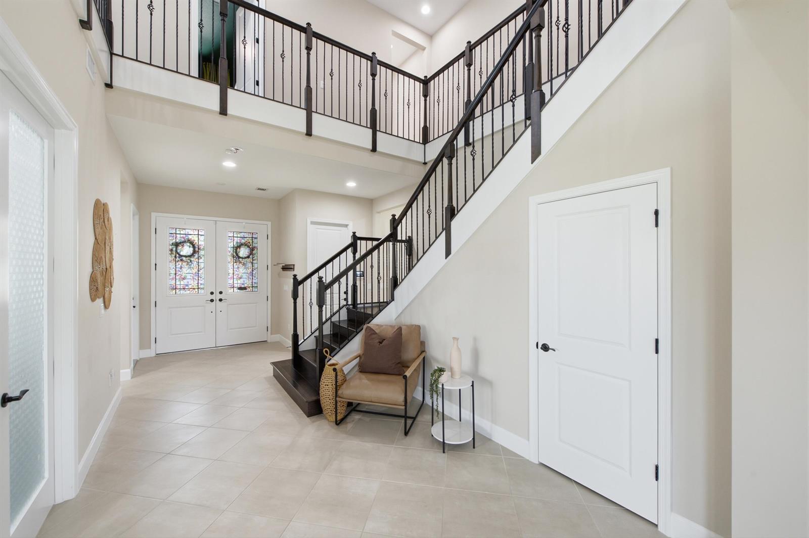 A bright foyer features a staircase with dark wood treads and a black metal railing — 14160 Lacebark Lane, Westlake FL 33470, WESTLAKE, FL