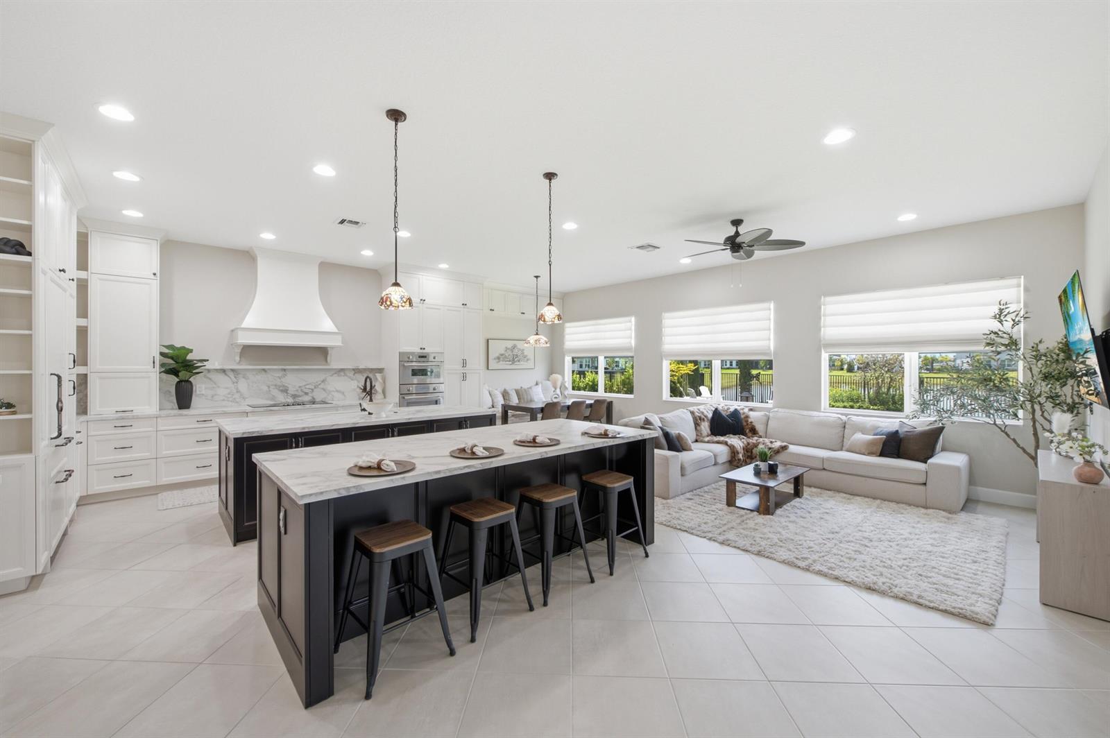A kitchen with a large island and seating opens into a living room with windows — 14160 Lacebark Lane, Westlake FL 33470, WESTLAKE, FL