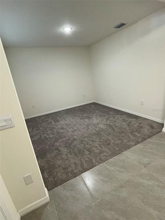 An empty room features gray carpeting, light-colored walls, and a tiled entryway — 15596 BLACK PEPPER LANE, ODESSA, FL