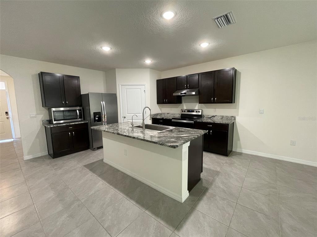 A kitchen features dark wood cabinets, granite countertops, and stainless steel appliances — 15596 BLACK PEPPER LANE, ODESSA, FL