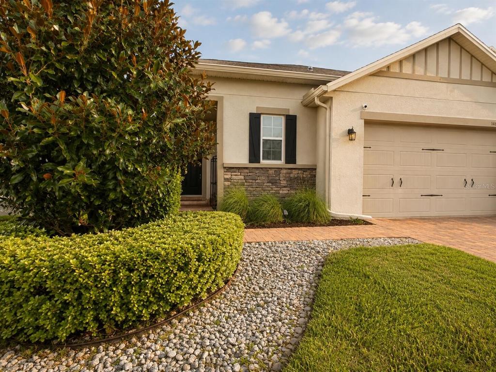 A single-story house exterior features a beige stucco facade, stone accents, and a paved driveway — 1463 SOURWOOD DRIVE, OCOEE, FL
