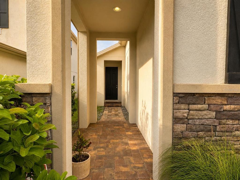 A paved walkway leads through a covered entryway to a dark front door — 1463 SOURWOOD DRIVE, OCOEE, FL