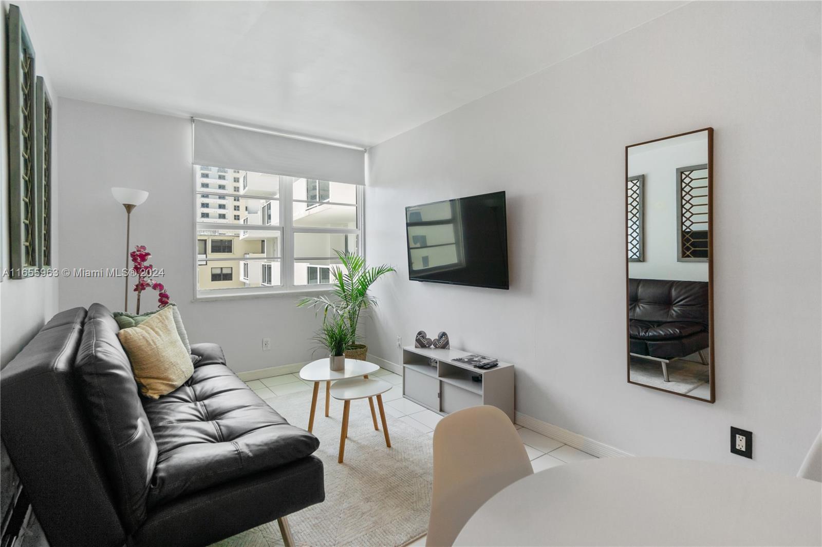A living room features a black sofa, a wall-mounted television, and a mirror on the wall — 100 Lincoln Rd # 924, Miami Beach FL 33139, MIAMI BEACH, FL