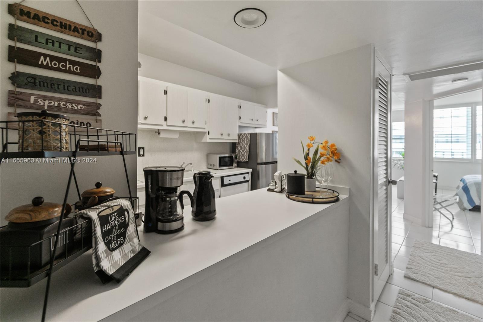 A kitchen with white cabinets and a breakfast bar overlooks a bedroom with tiled floors — 100 Lincoln Rd # 924, Miami Beach FL 33139, MIAMI BEACH, FL