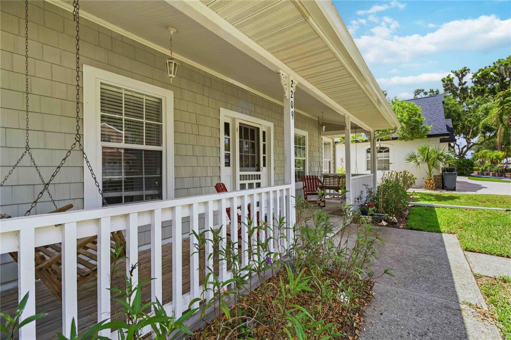 A covered front porch with a white railing, a porch swing, and gray shingle siding — 2209 68TH DRIVE E, ELLENTON, FL