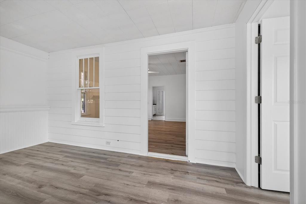 A room with white shiplap walls, wood-look flooring, and a doorway leading to another room — 2211 22ND AVENUE S, ST PETERSBURG, FL