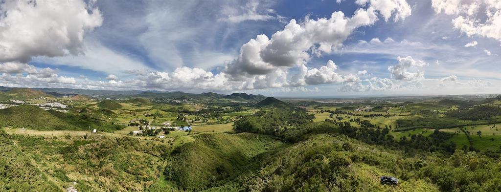 A wide-angle aerial view shows a vast, hilly landscape with green fields and distant mountains — 2565 PR545, COAMO, PR
