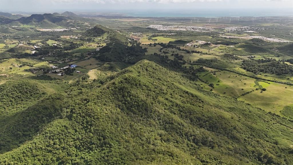 An aerial view shows a lush green mountain landscape overlooking a distant coastal plain — 2565 PR545, COAMO, PR