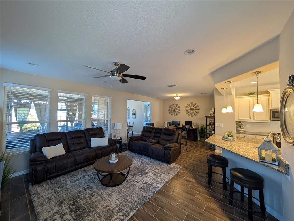 An open-concept living room features dark leather furniture, tile flooring, and an adjacent kitchen island — 4341 NW 57TH AVENUE, OCALA, FL