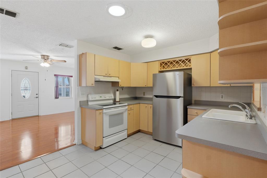 A kitchen with light wood cabinets, gray countertops, stainless steel appliances, and white tile flooring — 6130 17TH STREET, ZEPHYRHILLS, FL
