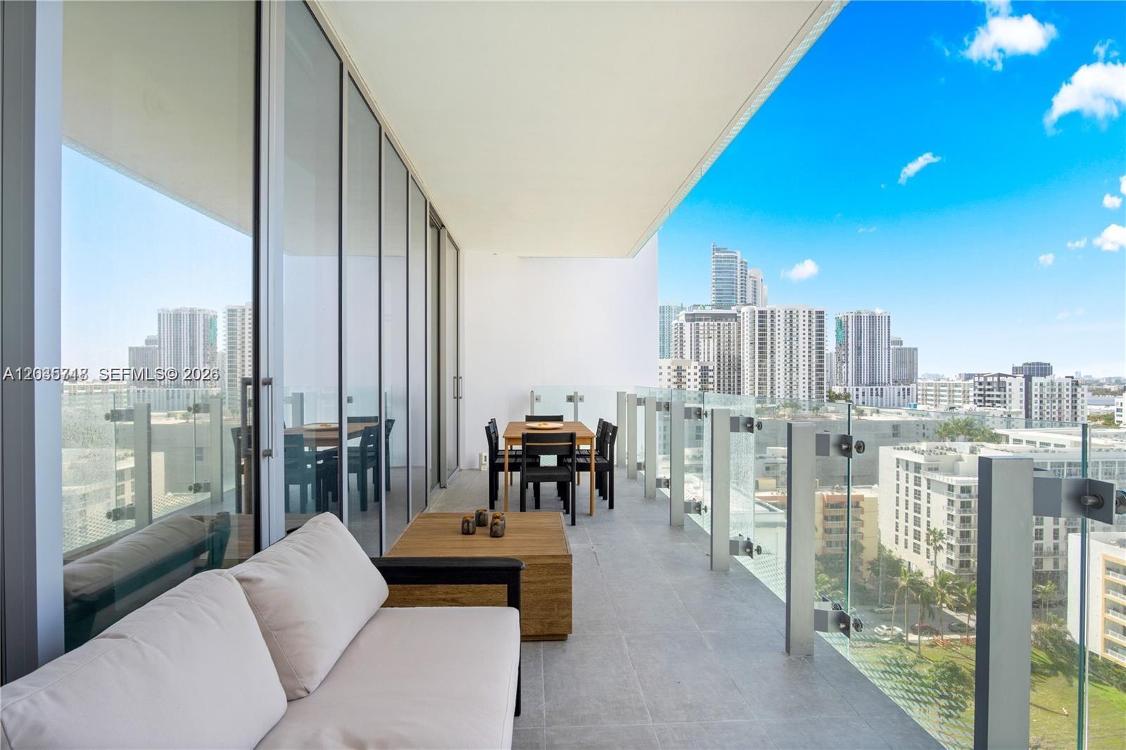 A modern balcony features a sofa, dining set, and glass railings overlooking a city skyline — 700 NE 26th Ter # 1405, Miami FL 33137, MIAMI, FL