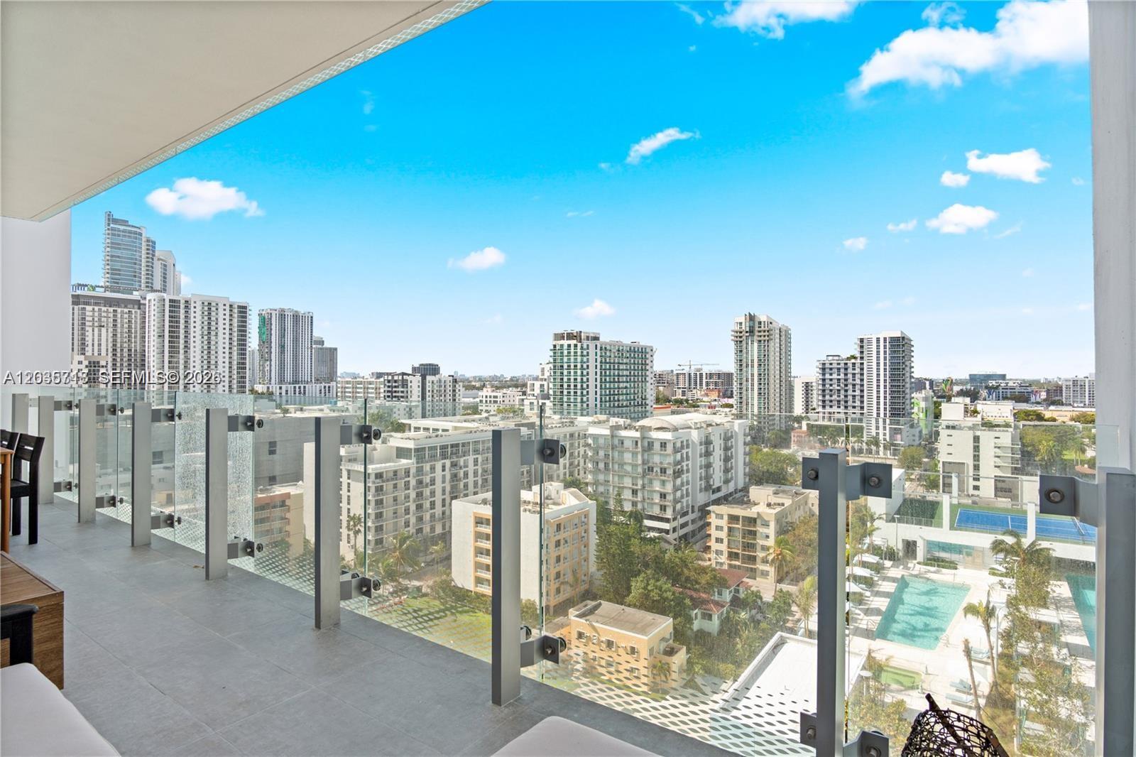 A high-rise balcony with a glass railing overlooks a dense city skyline and swimming pool — 700 NE 26th Ter # 1405, Miami FL 33137, MIAMI, FL