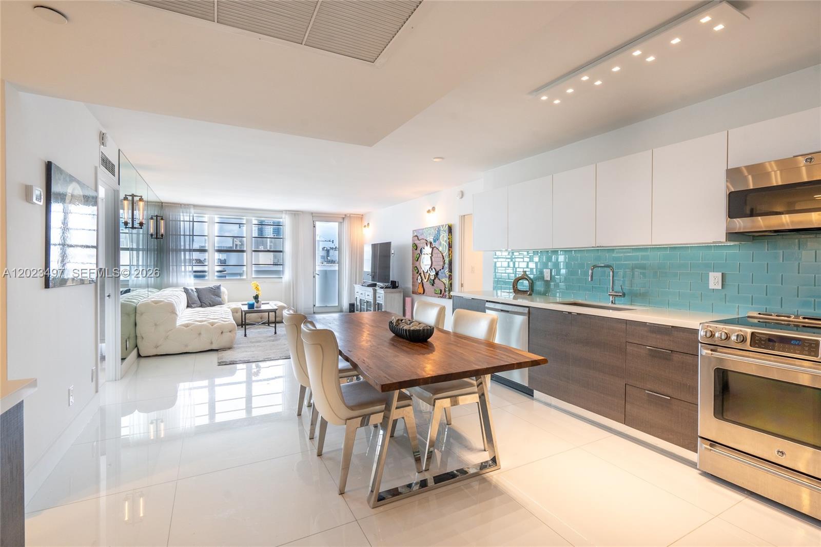 A modern open-concept kitchen and dining area features white cabinets, teal backsplash, and tile flooring — 100 Lincoln Rd # 1523, Miami Beach FL 33139, MIAMI BEACH, FL