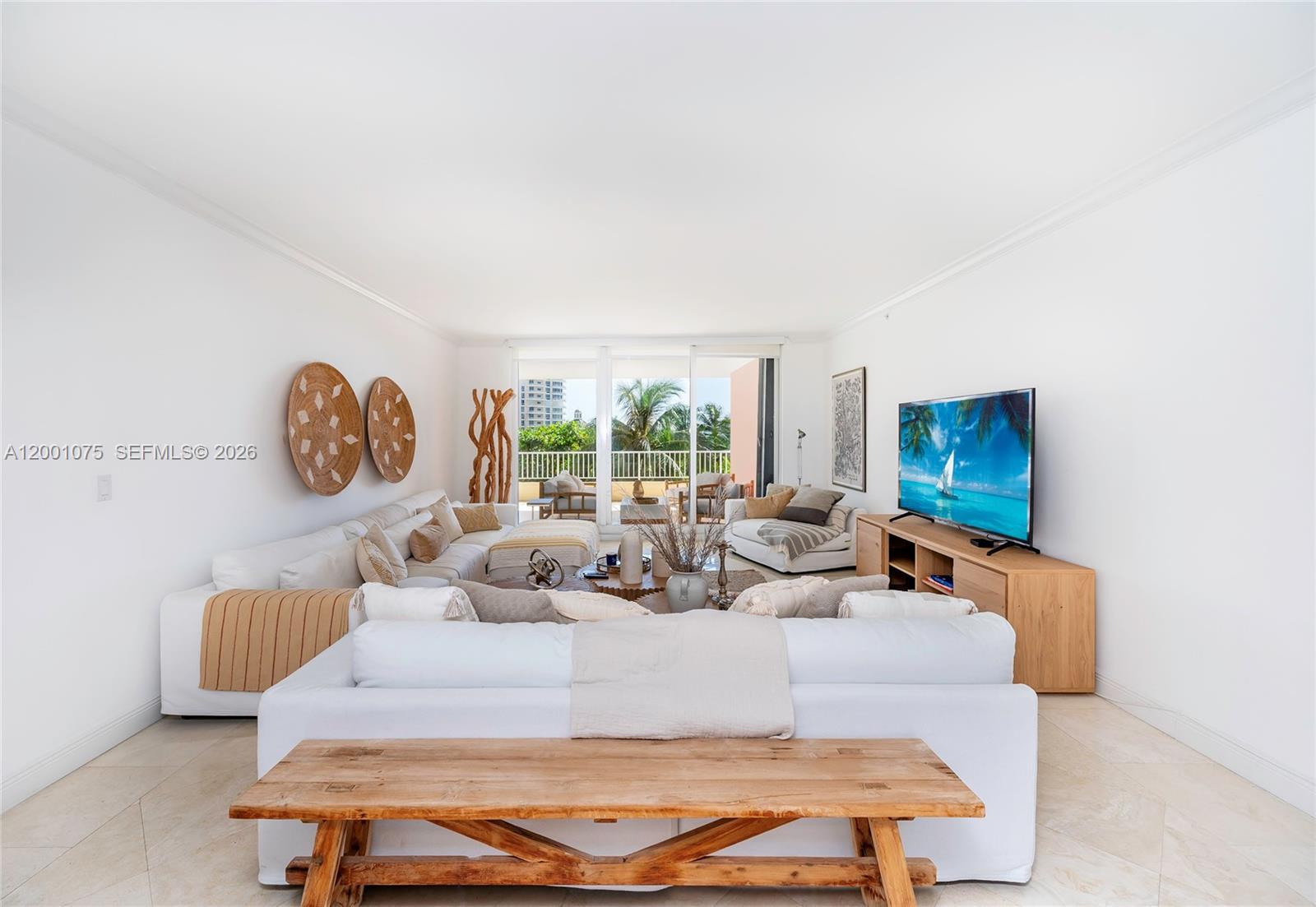 A bright living room features white sofas, a wooden bench, and a balcony with palm trees — 789 Crandon Blvd # 502, Key Biscayne FL 33149, KEY BISCAYNE, FL