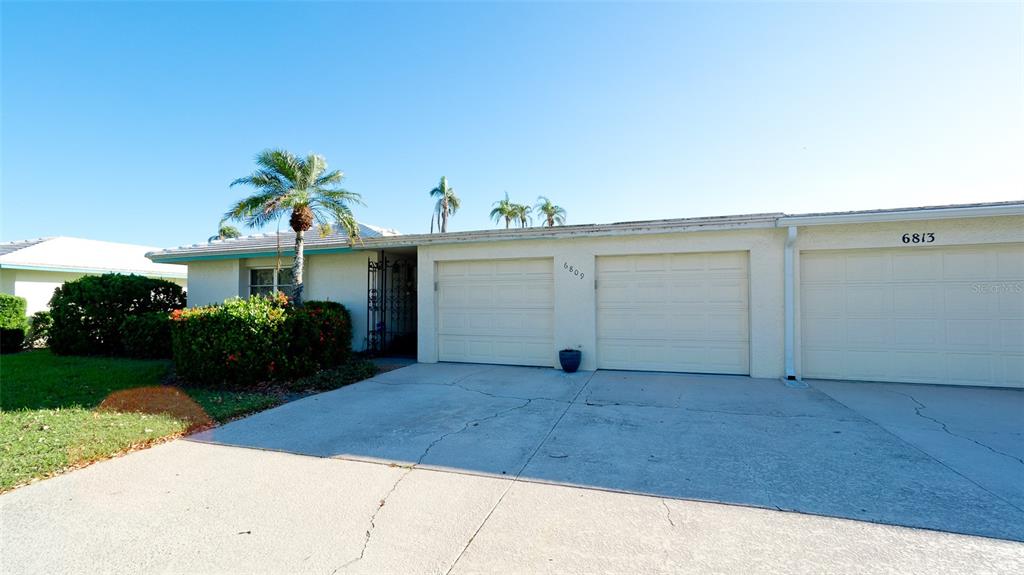 A single-story house exterior features a two-car garage, a concrete driveway, and palm trees — 6809 9TH AVENUE W UNIT 523, BRADENTON, FL