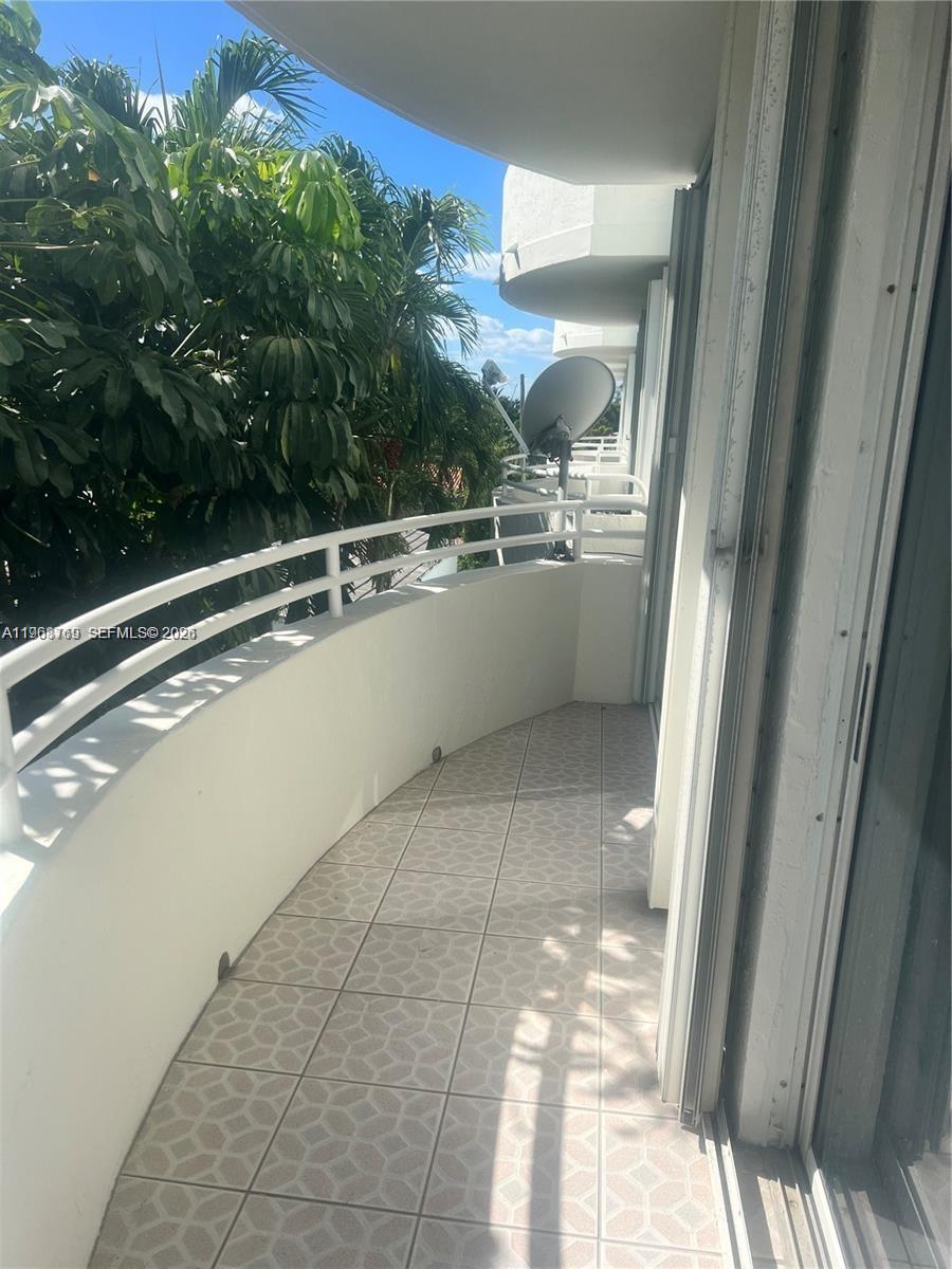 A curved balcony features light-colored patterned floor tiles and a white metal railing — 9156 Collins Ave # 204, Surfside FL 33154, SURFSIDE, FL