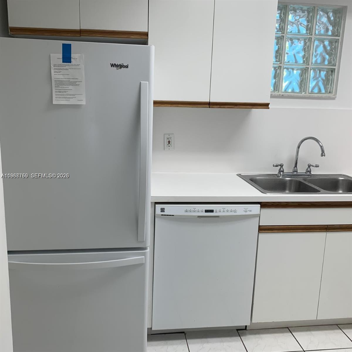 A white kitchen features a Whirlpool refrigerator, dishwasher, double sink, and glass block window — 9156 Collins Ave # 204, Surfside FL 33154, SURFSIDE, FL