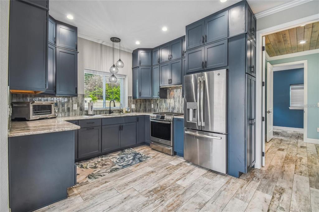 A kitchen features dark blue cabinets, stainless steel appliances, and wood-look tile flooring — 8574 SW SAND CRANE - LOT 53 CIRCLE, ARCADIA, FL