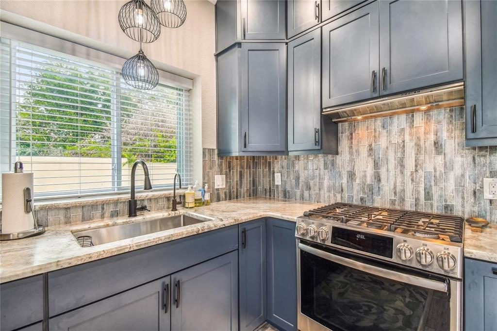 A kitchen features blue cabinets, a stainless steel sink, a gas range, and tiled backsplash — 8574 SW SAND CRANE - LOT 53 CIRCLE, ARCADIA, FL