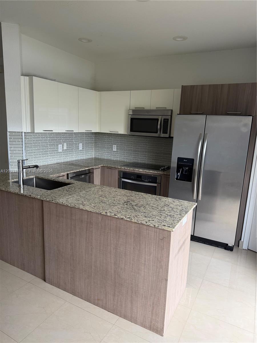 A kitchen features light wood cabinets, white upper cabinets, granite countertops, and stainless steel appliances — 10803 NW 83rd St # 1, Doral FL 33178, DORAL, FL