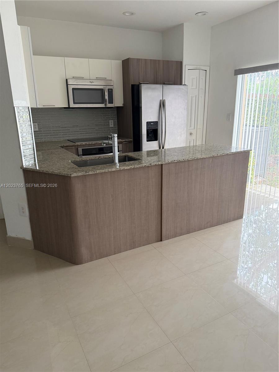 A kitchen features a granite-topped island, stainless steel appliances, and light-colored tile flooring — 10803 NW 83rd St # 1, Doral FL 33178, DORAL, FL