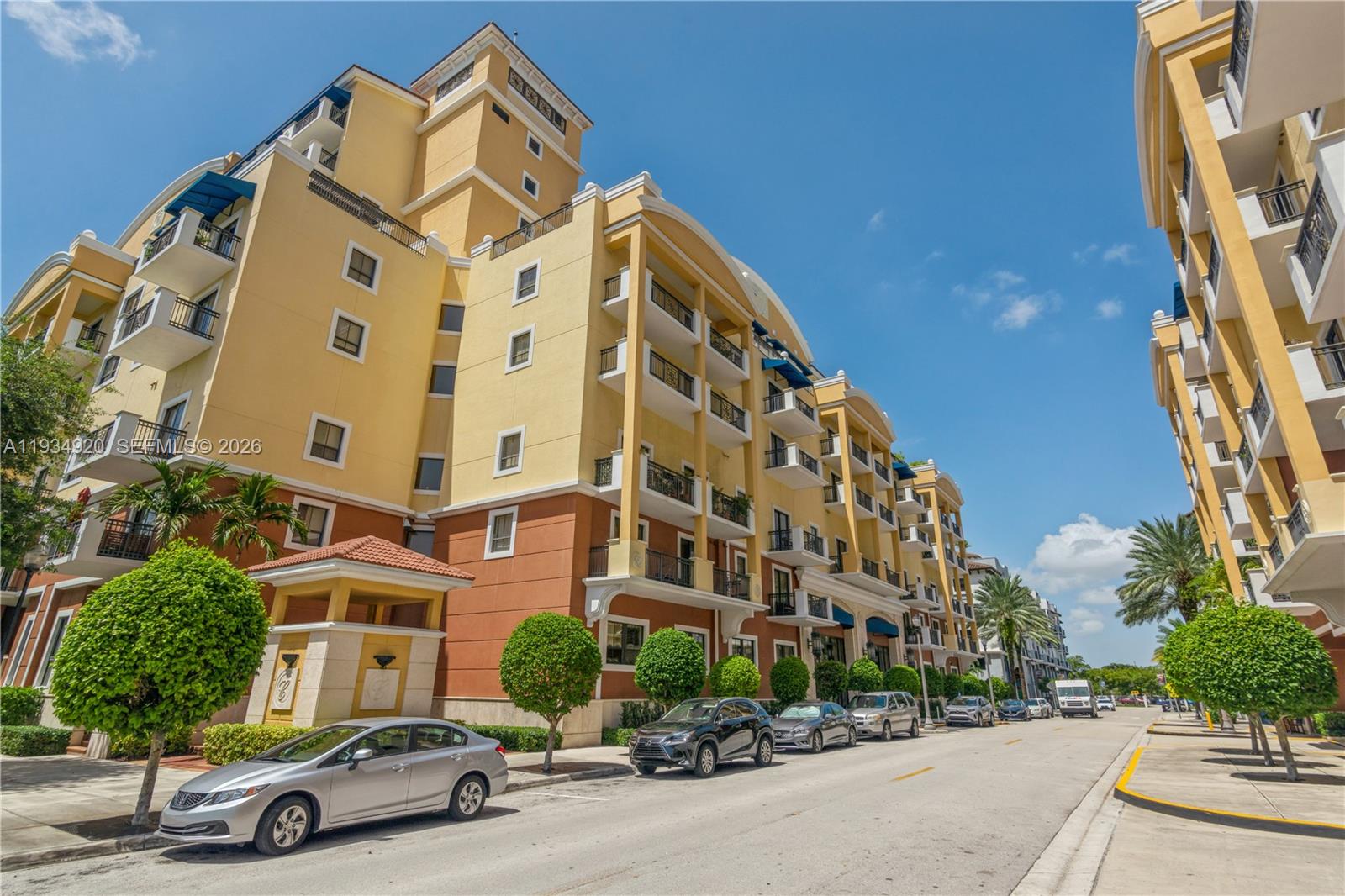 A multi-story yellow and brown apartment building stands along a street with parked cars — 8395 SW 73rd Ave # 417, Miami FL 33143, MIAMI, FL