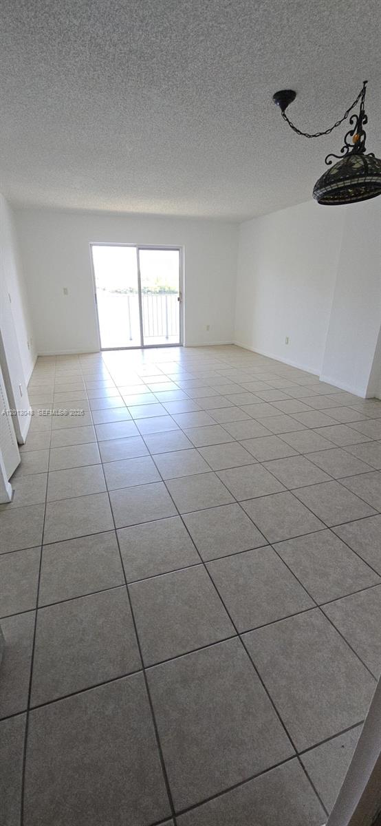 An empty room features light-colored tile flooring, white walls, and a sliding glass balcony door — 8240 SW 210th St # 214, Cutler Bay FL 33189, CUTLER BAY, FL