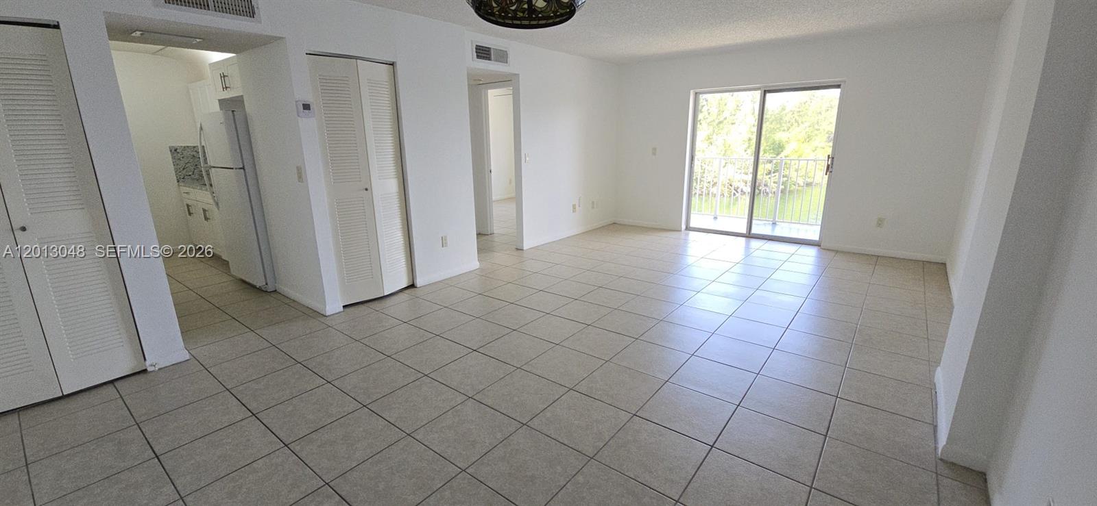 An open-concept living area features light-colored tile flooring, white walls, and a sliding glass door — 8240 SW 210th St # 214, Cutler Bay FL 33189, CUTLER BAY, FL