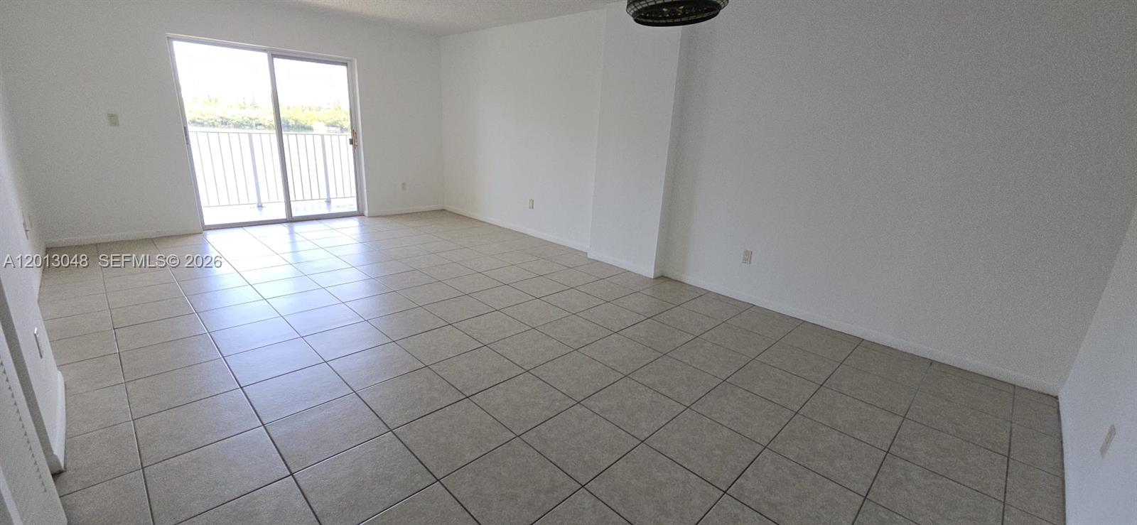 An empty living room features light-colored tile flooring, white walls, and a sliding glass door — 8240 SW 210th St # 214, Cutler Bay FL 33189, CUTLER BAY, FL