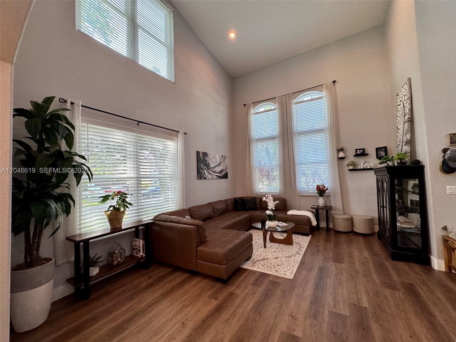 A living room features high ceilings, large windows, a brown sectional sofa, and wood flooring — 12917 SW 23rd St, Miramar FL 33027, MIRAMAR, FL