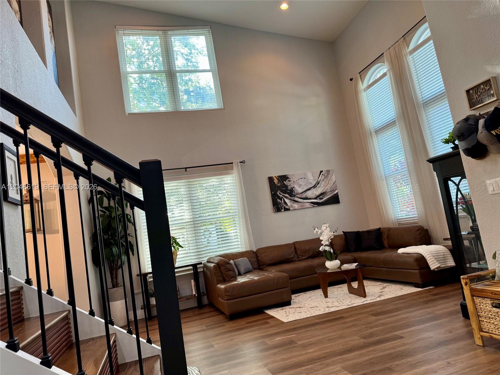 A living room with high ceilings, a brown sectional sofa, and a staircase with railing — 12917 SW 23rd St, Miramar FL 33027, MIRAMAR, FL