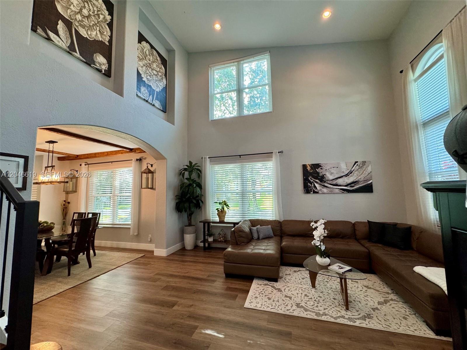 A high-ceilinged living room features a brown sectional sofa, wood flooring, and an arched entryway — 12917 SW 23rd St, Miramar FL 33027, MIRAMAR, FL