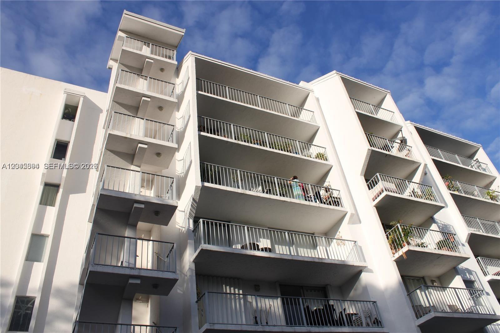 A low-angle view of a white multi-story apartment building with balconies and exterior stairwells — 700 NE 63rd St, Miami FL 33138, MIAMI, FL