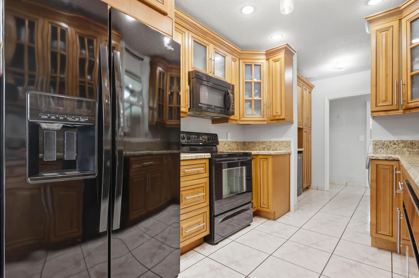 A kitchen features wood cabinets, granite countertops, black appliances, and light-colored tile flooring — 6448 Custer Street, Hollywood FL 33024, HOLLYWOOD, FL
