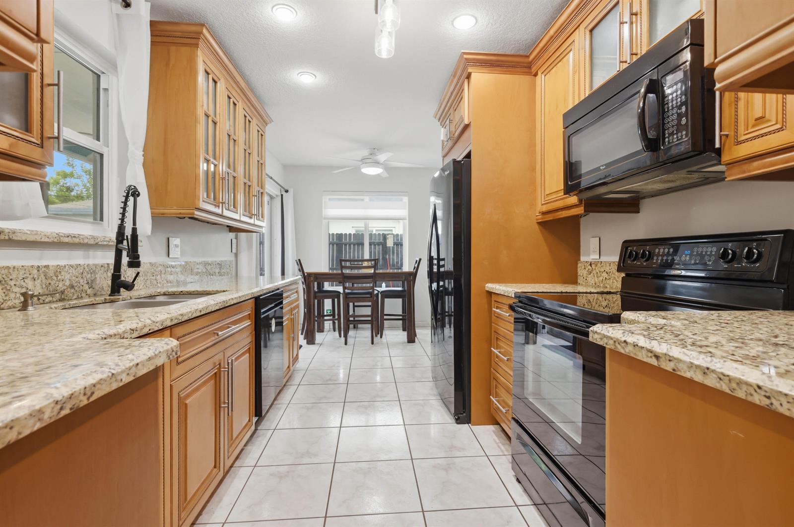 A kitchen with wood cabinets, granite countertops, black appliances, and a dining area beyond — 6448 Custer Street, Hollywood FL 33024, HOLLYWOOD, FL