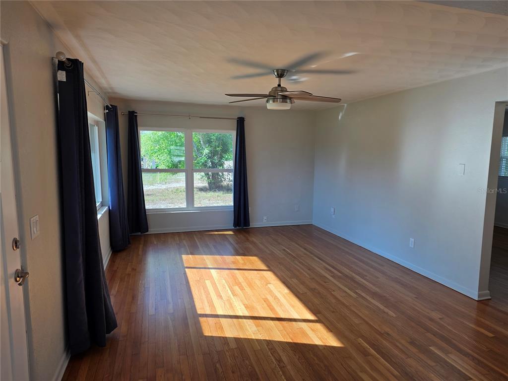 A living room features hardwood floors, a ceiling fan, and windows with dark blue curtains — 915 NORMAN DRIVE, MOUNT DORA, FL