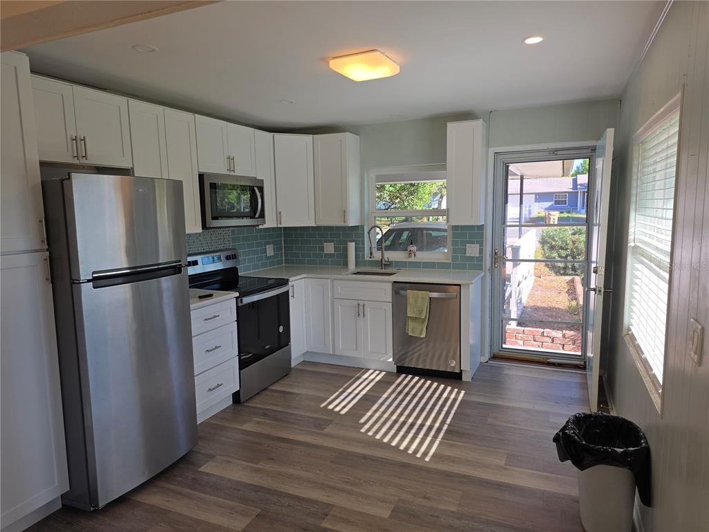 A kitchen features white cabinets, stainless steel appliances, a blue tile backsplash, and wood-look flooring — 915 NORMAN DRIVE, MOUNT DORA, FL