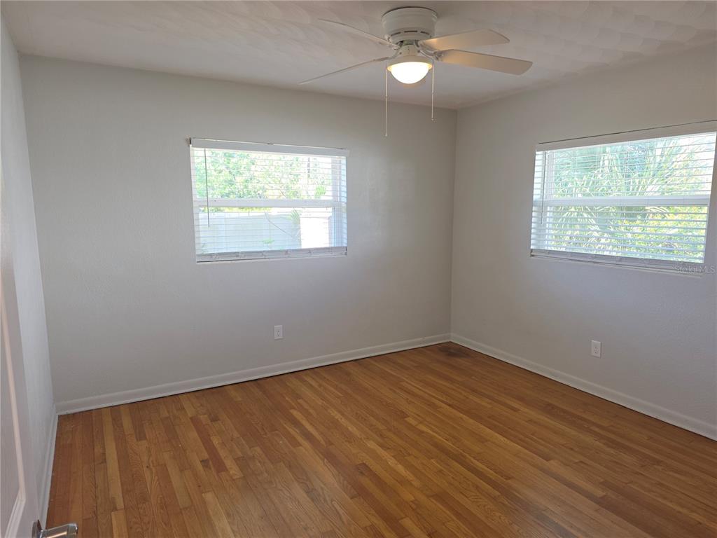 A bedroom with light gray walls, hardwood floors, two windows with blinds, and a ceiling fan — 915 NORMAN DRIVE, MOUNT DORA, FL