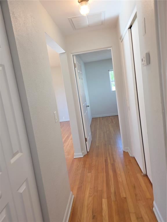 A hallway with hardwood floors leads to an open doorway showing a bedroom with a window — 915 NORMAN DRIVE, MOUNT DORA, FL