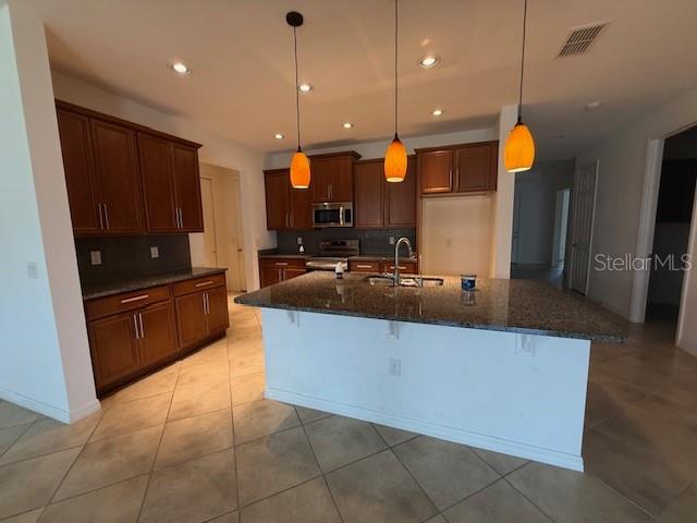 A kitchen features dark wood cabinets, a granite-topped island, and three hanging pendant lights — 1284 BONITA CANYON DRIVE, POINCIANA, FL