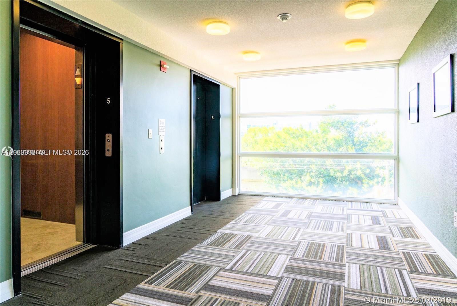 An elevator lobby features green walls, patterned carpet, and a large window overlooking trees — 816 NW 11th St # 801, Miami FL 33136, MIAMI, FL