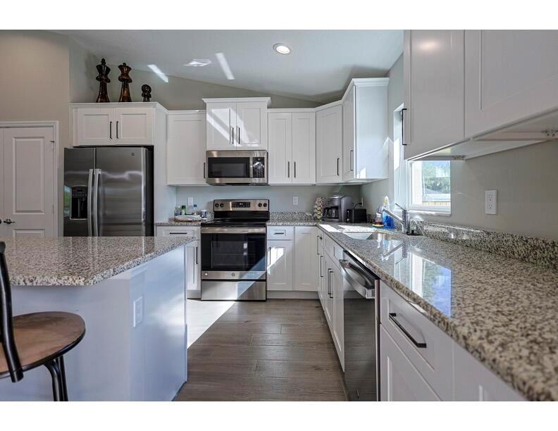 A kitchen features white cabinets, granite countertops, stainless steel appliances, and wood-look flooring — 6106 Bamboo Drive, Fort Pierce FL 34982, FORT PIERCE, FL