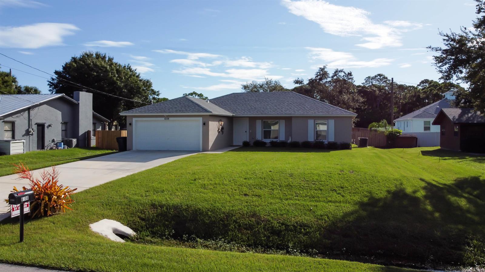 A single-story house with a two-car garage, light-colored siding, and a large front lawn — 6106 Bamboo Drive, Fort Pierce FL 34982, FORT PIERCE, FL