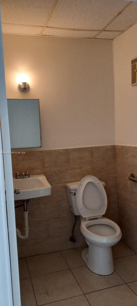 A small bathroom features a wall-mounted sink, a white toilet, and beige tiled walls — 2067 W 62nd St, Hialeah FL 33016, HIALEAH, FL