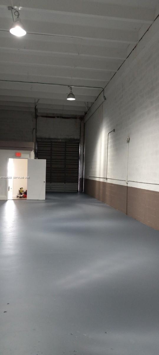An empty warehouse space features a gray concrete floor, white walls, and a roll-up door — 2067 W 62nd St, Hialeah FL 33016, HIALEAH, FL