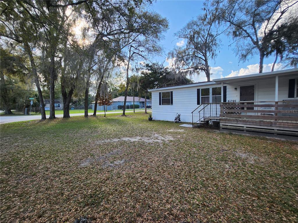 A white mobile home with a wooden deck stands on a grassy, tree-filled lot — 6091 SE 114TH STREET ROAD, BELLEVIEW, FL